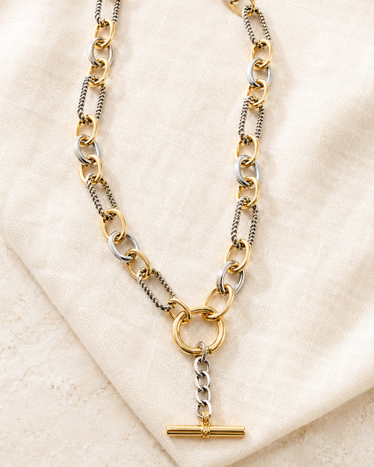 Plot Twist mixed metal Y necklace with gold and silver links and T-bar pendant styled on ivory linen