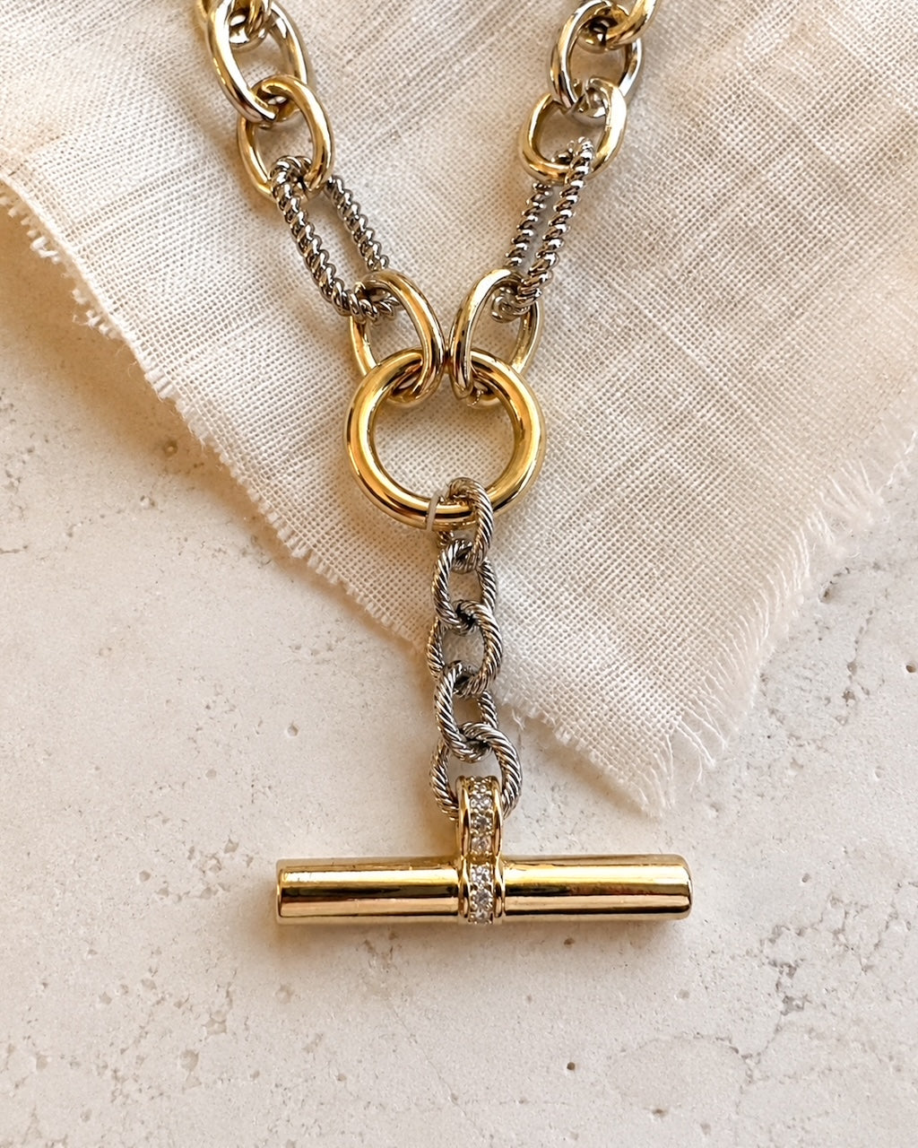 Close-up of the Plot Twist Necklace showing the gold T-bar, cubic zirconia detail and silver drop links