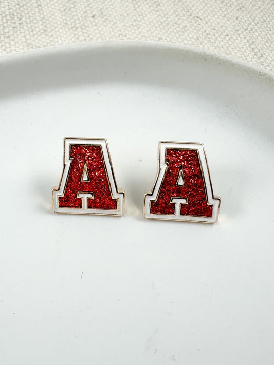 Red glitter letter A stud earrings with gold trim displayed on a white dish