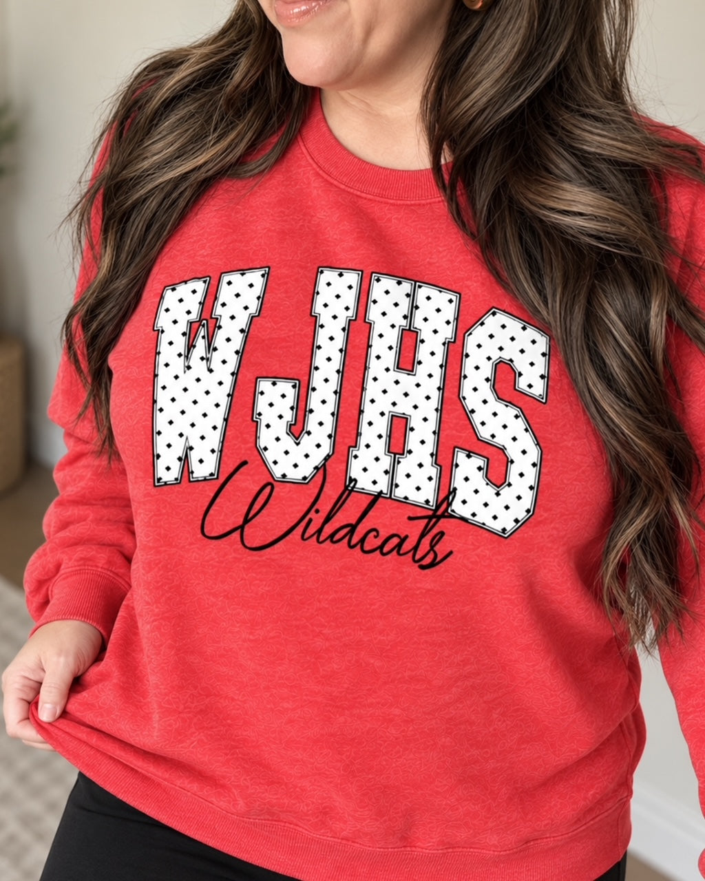 Woman wearing a heather red WJHS Wildcats crewneck sweatshirt with white polka-dot lettering and black script design.