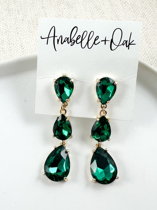 Emerald green teardrop crystal earrings with layered drop design and gold-tone hardware shown on a branded card