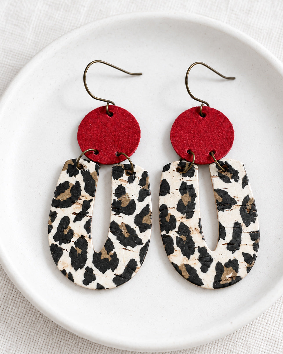 Red Velvet Leopard Earrings displayed on a matte white dish with red suede and leopard-print cork details