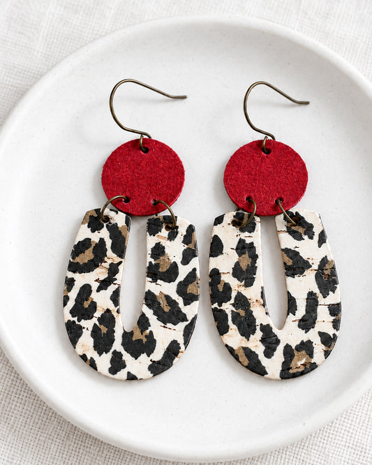 Red Velvet Leopard Earrings displayed on a matte white dish with red suede and leopard-print cork details