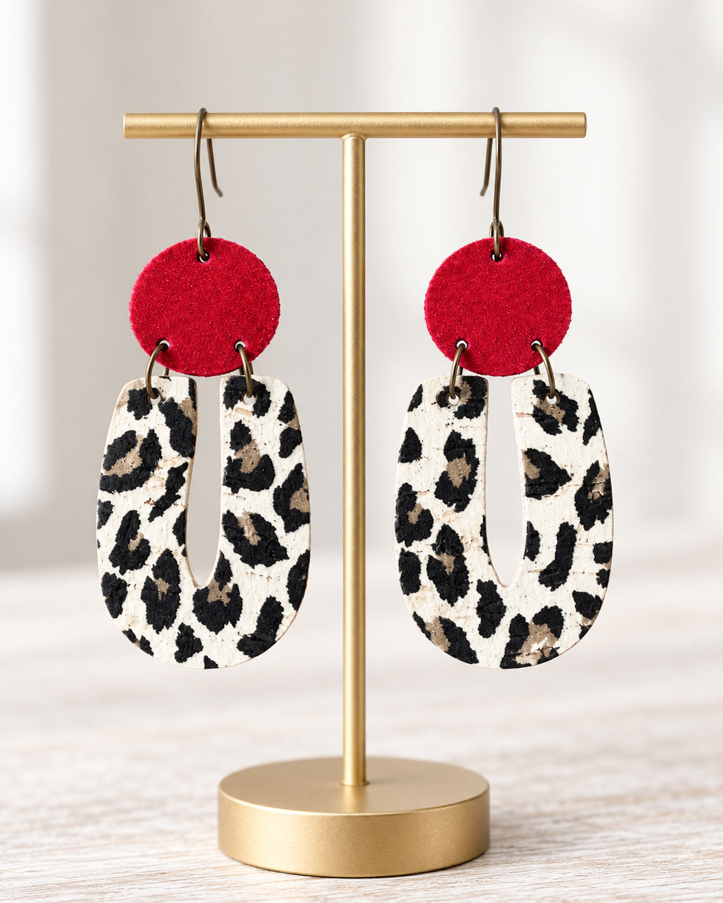Red Velvet Leopard Earrings hanging from a matte gold jewelry stand against a softly lit neutral background