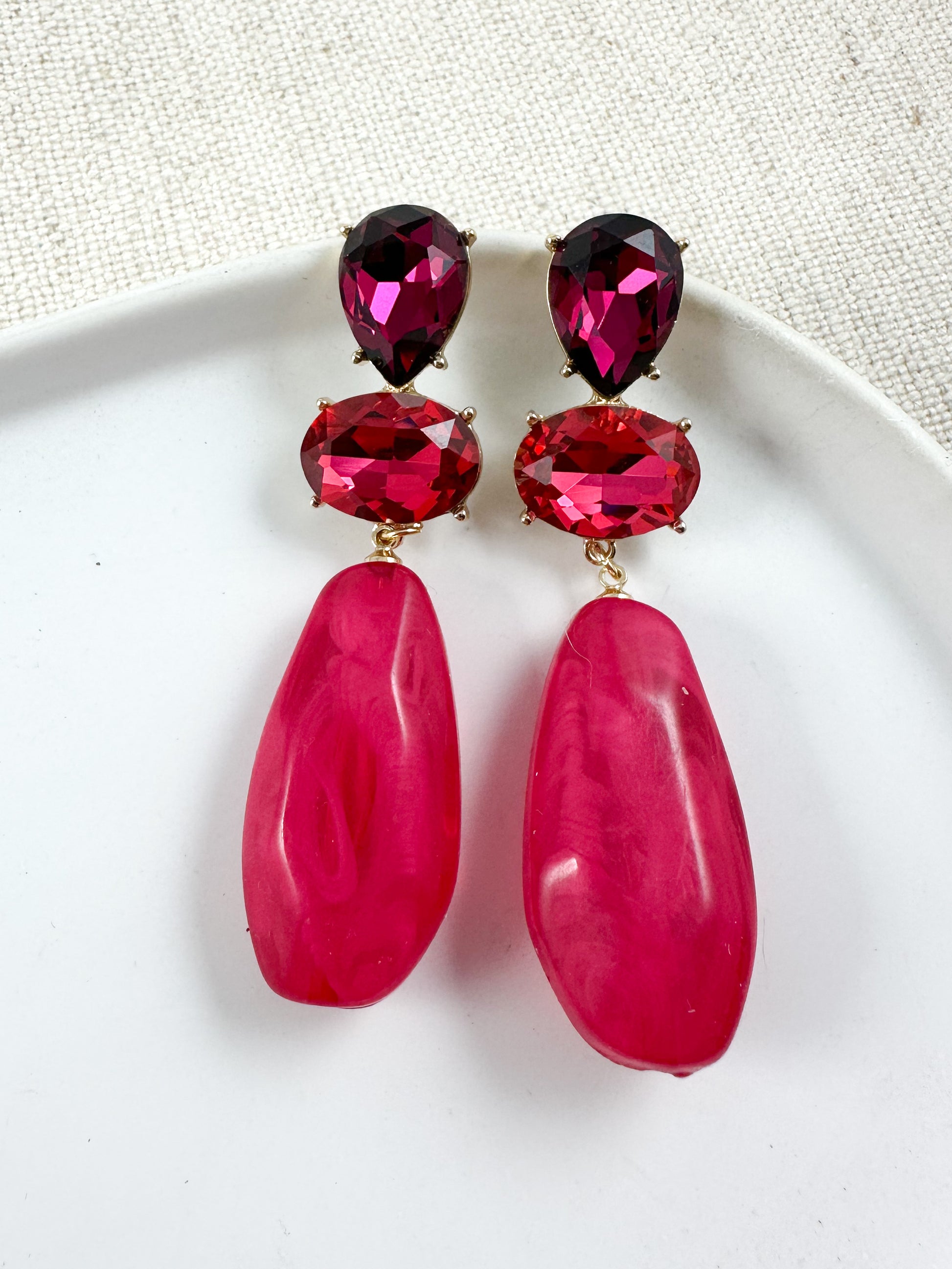 Fuchsia gemstone-style drop earrings with gold hardware photographed on a white plate