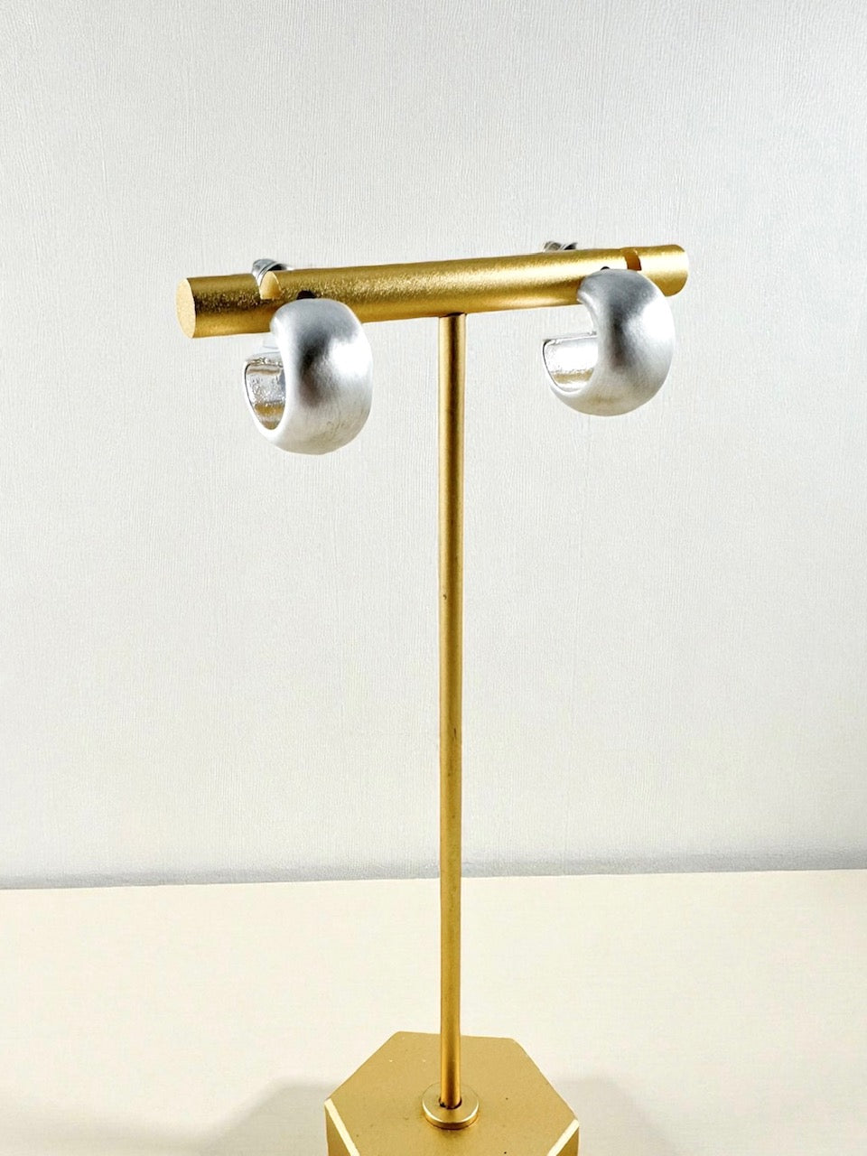 small matte silver curved hoop earrings displayed on a gold stand
