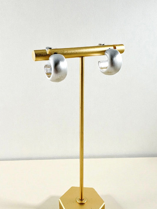 small matte silver curved hoop earrings displayed on a gold stand
