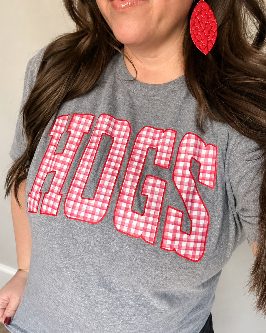 Woman wearing a heather gray graphic tee with oversized HOGS lettering in red and white gingham, outlined in red.