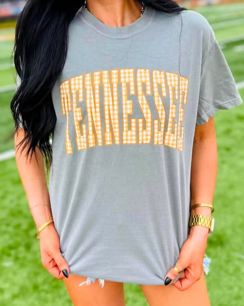 Woman wearing a heather gray tee with oversized TENNESSEE lettering in orange and white gingham.