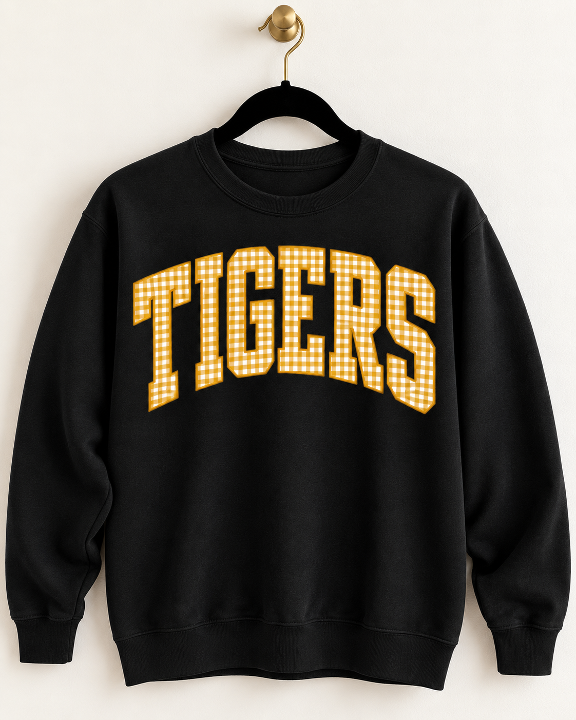 Black crewneck sweatshirt with oversized TIGERS lettering in gold and white gingham, hanging on a black velvet hanger.