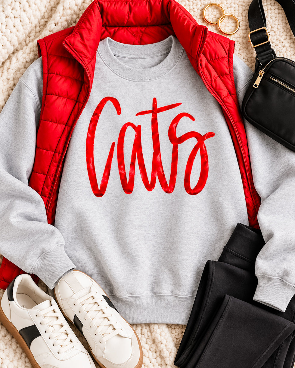 Gray Cats sweatshirt with metallic red lettering styled with a red puffer vest, black pants, white sneakers, and black bag.