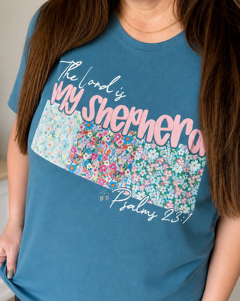 Woman wearing the Shepherd's Garden Tee featuring a floral "The Lord Is My Shepherd" Psalm 23 design on a heather deep teal Bella Canvas shirt.