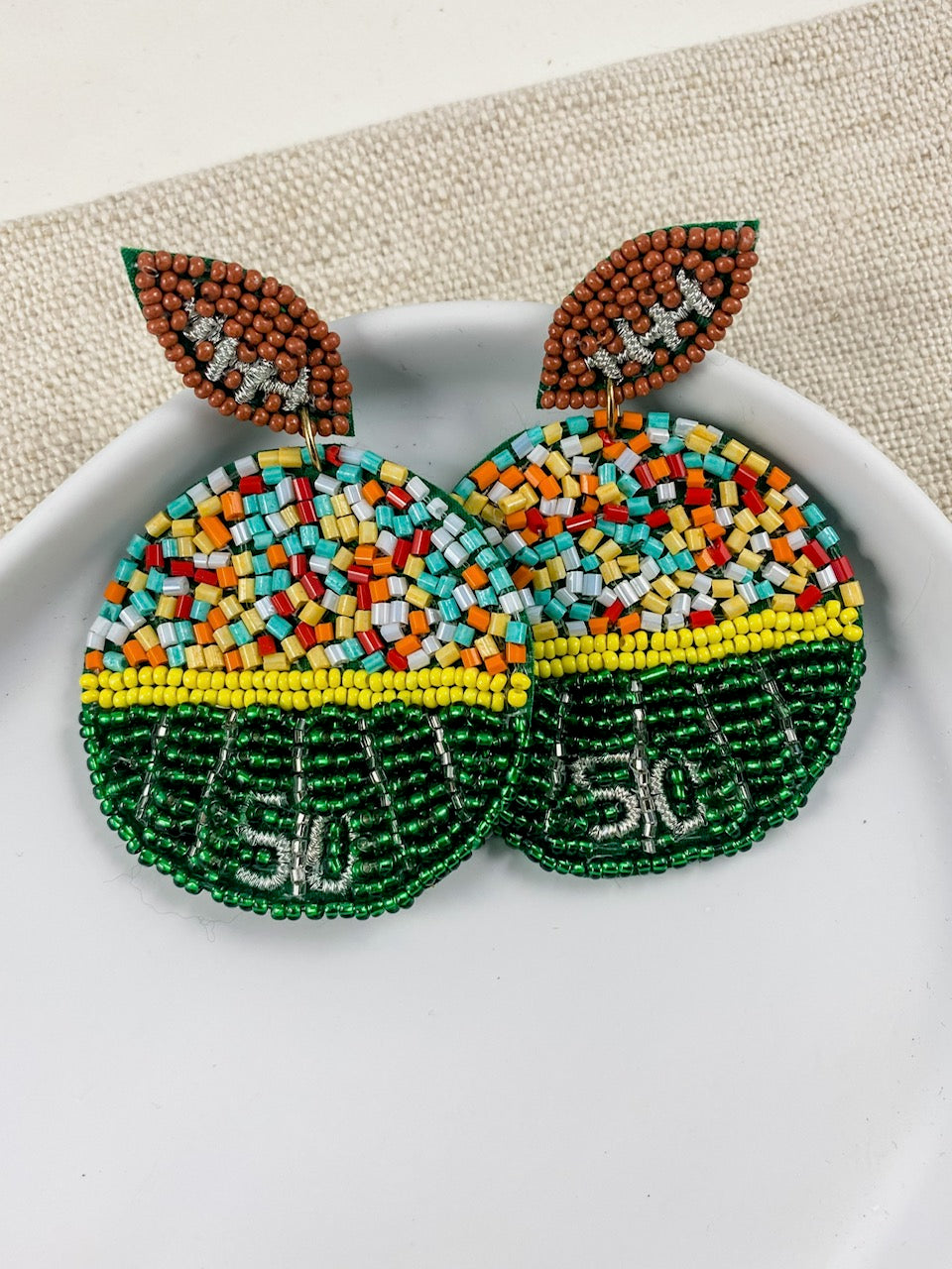 Sideline Spirit football field seed bead earrings displayed in a white ceramic dish on neutral linen.