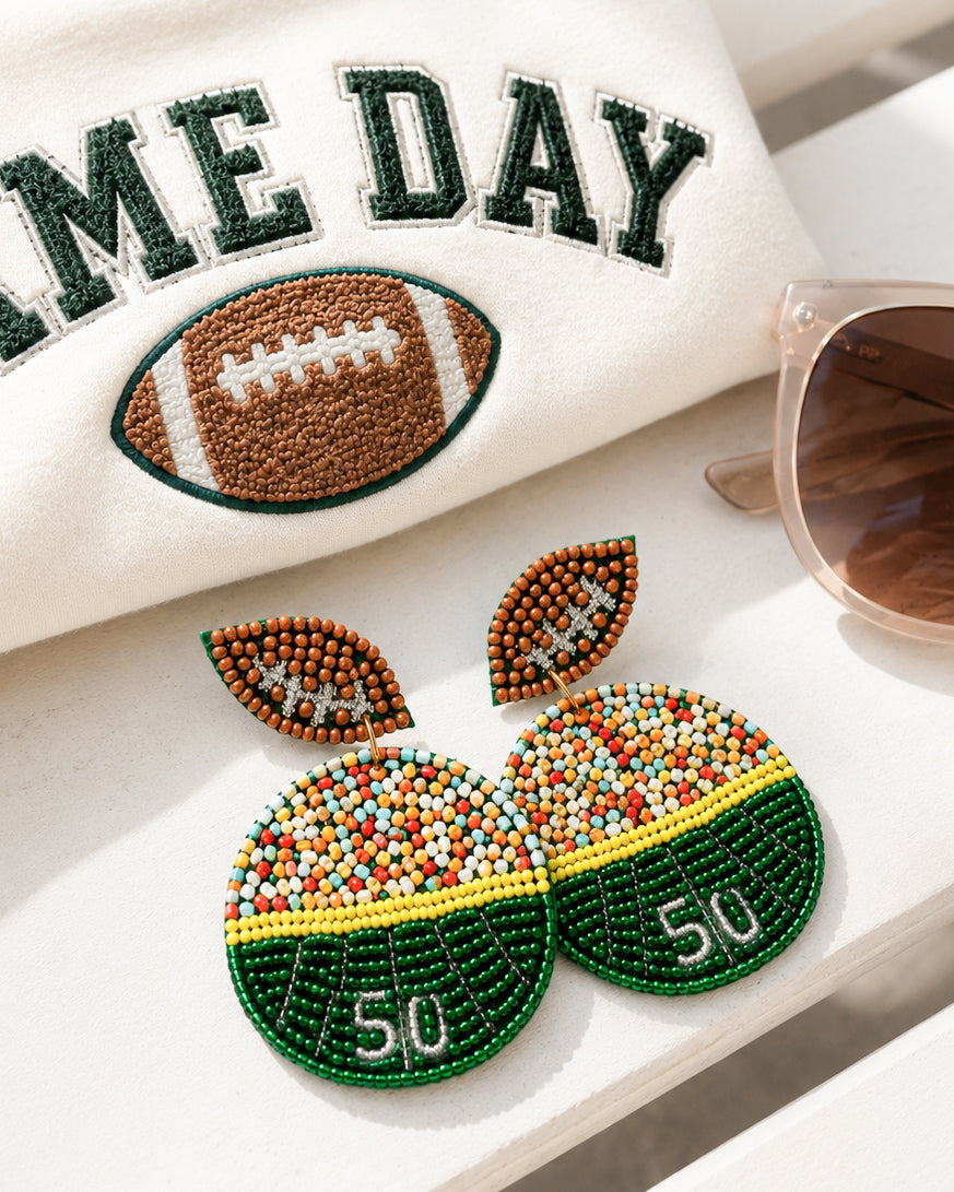 Sideline Spirit football field seed bead statement earrings styled with a game day sweatshirt and sunglasses.