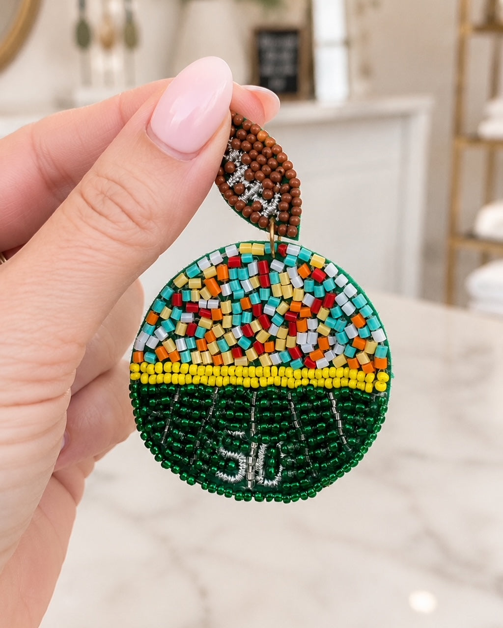 Hand holding Sideline Spirit football field seed bead earrings to show their 2.5-inch statement size.
