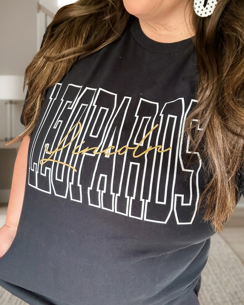 Woman wearing a black Lincoln Leopards graphic tee with white outlined varsity lettering and gold script.