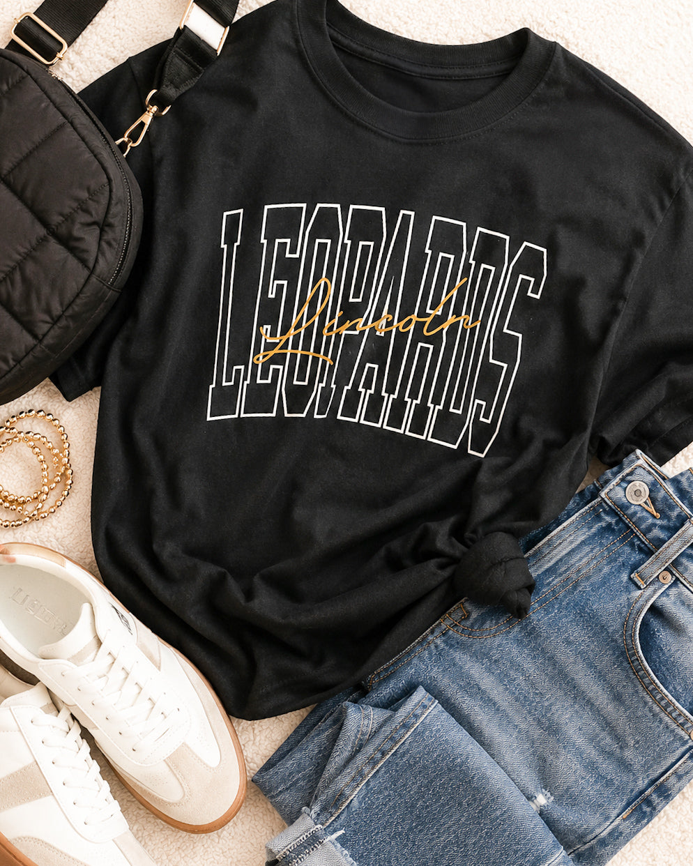 Black short-sleeve Lincoln Leopards graphic tee with white outlined varsity lettering and gold script on a black hanger.