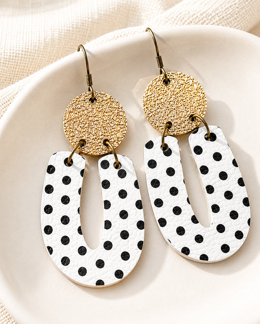 Black and white polka dot earrings with textured matte gold glitter tops displayed on a white ceramic dish.