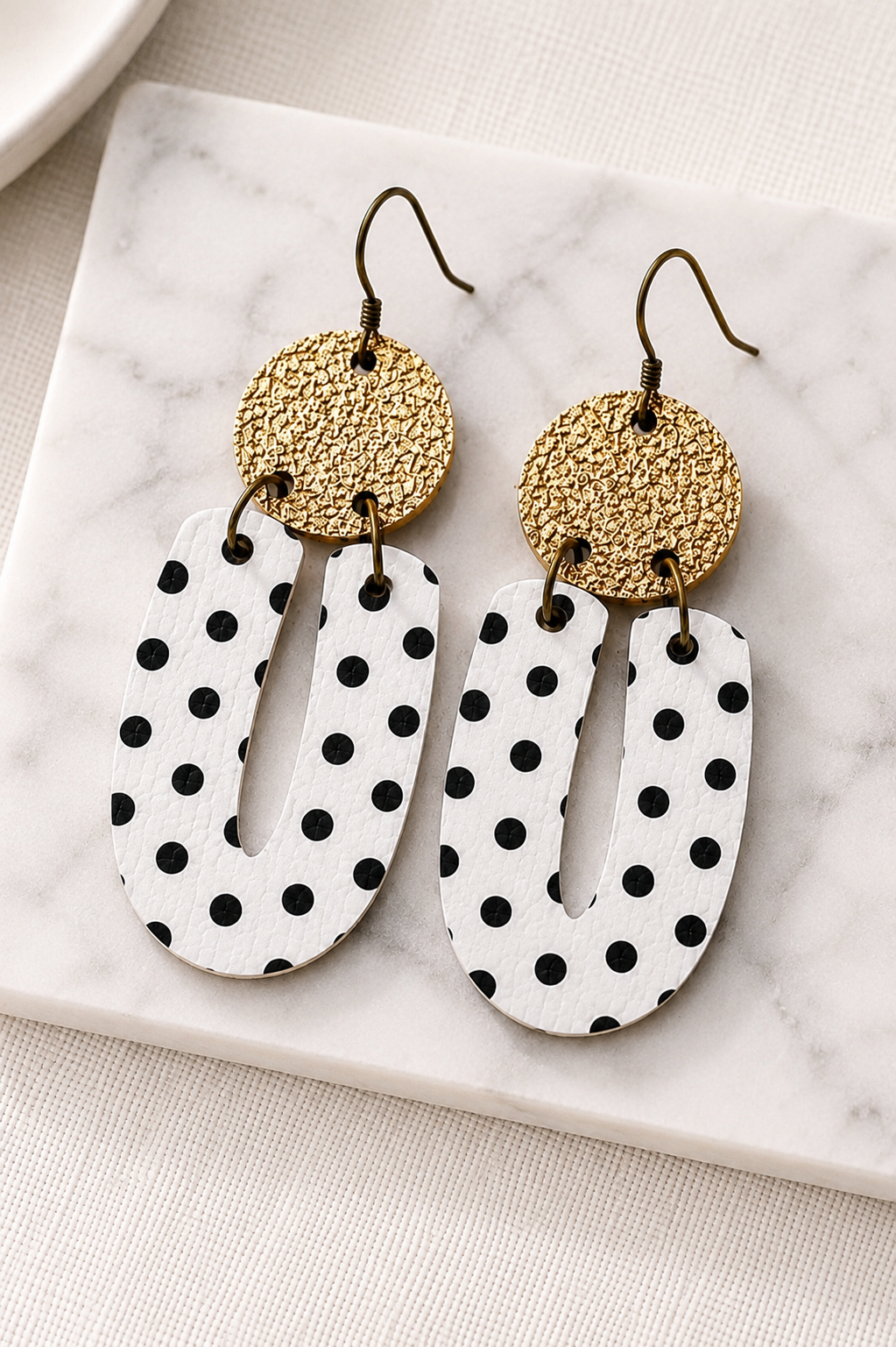 Black and white polka dot earrings displayed on a soft neutral surface, showing the lightweight statement shape and polka dot print.