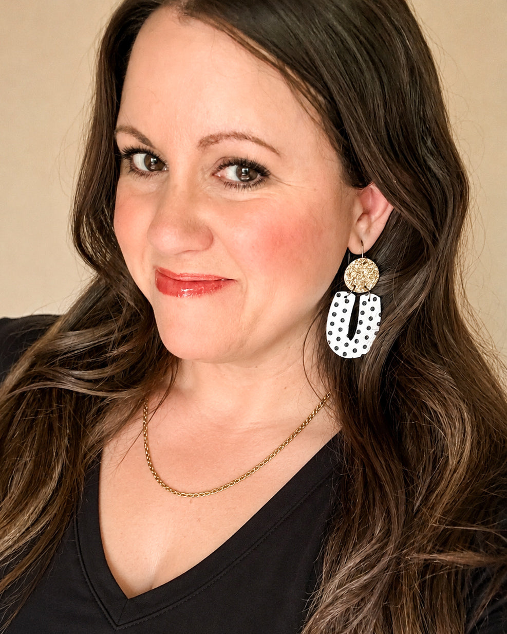 Woman modeling black and white polka dot earrings with matte gold glitter tops and a simple black V-neck top.