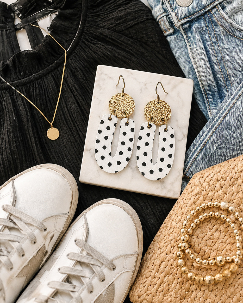 Black and white polka dot earrings styled with denim, a black top, white sneakers, and gold accessories.