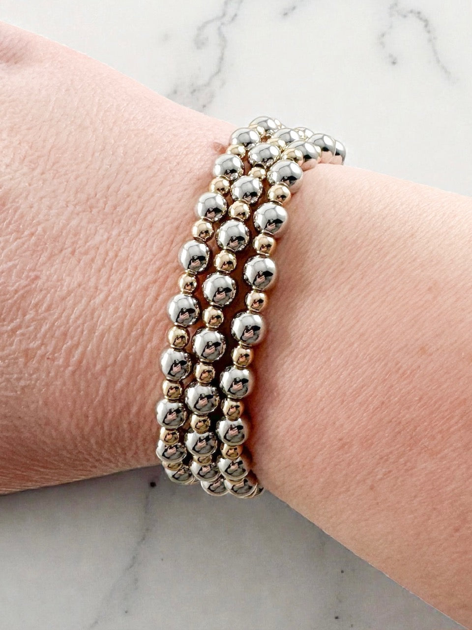Three mixed metal stretch bracelets with polished silver beads and gold spacer beads stacked together on a wrist.