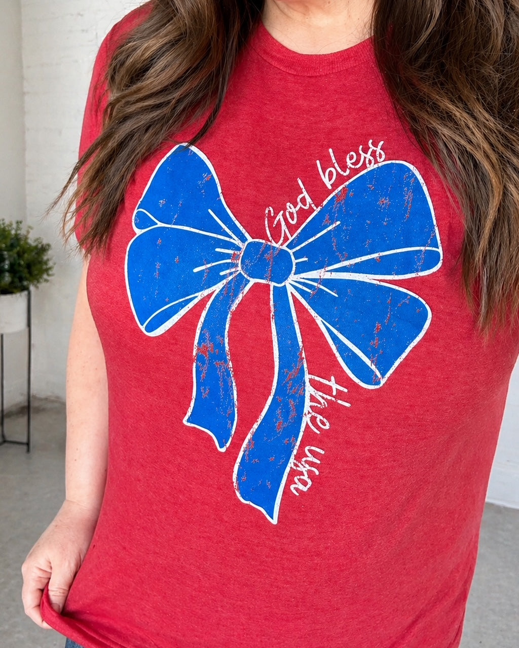 Woman wearing the Small Town USA graphic tee featuring a distressed patriotic bow design on a soft heather red shirt