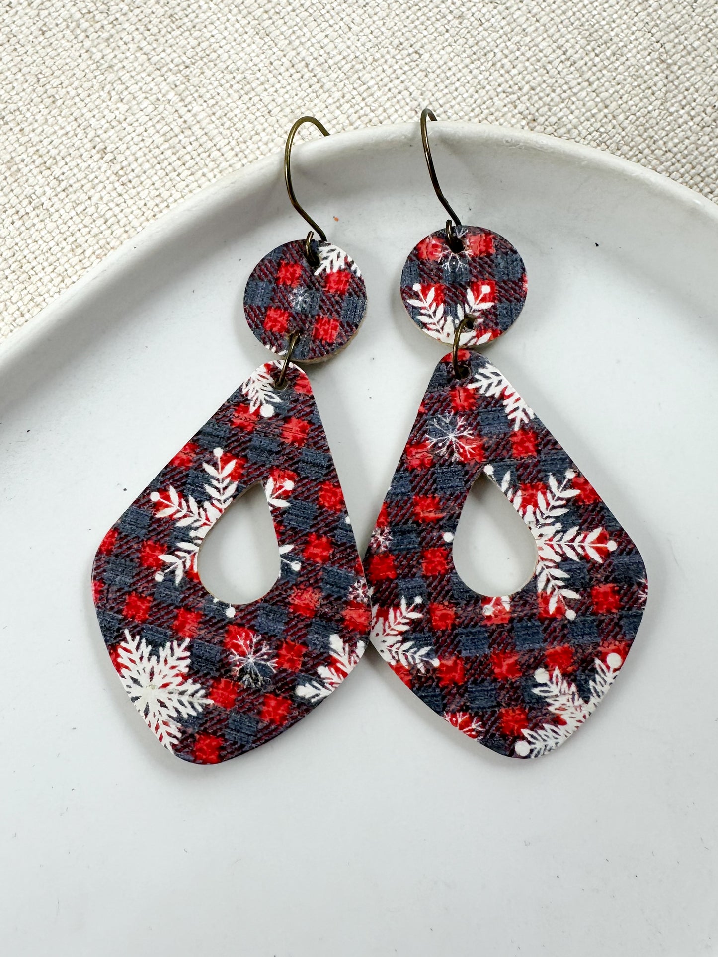 Snowflake & Flannel Cork teardrop statement earrings with red and navy flannel checks and white snowflakes displayed on a white tray.