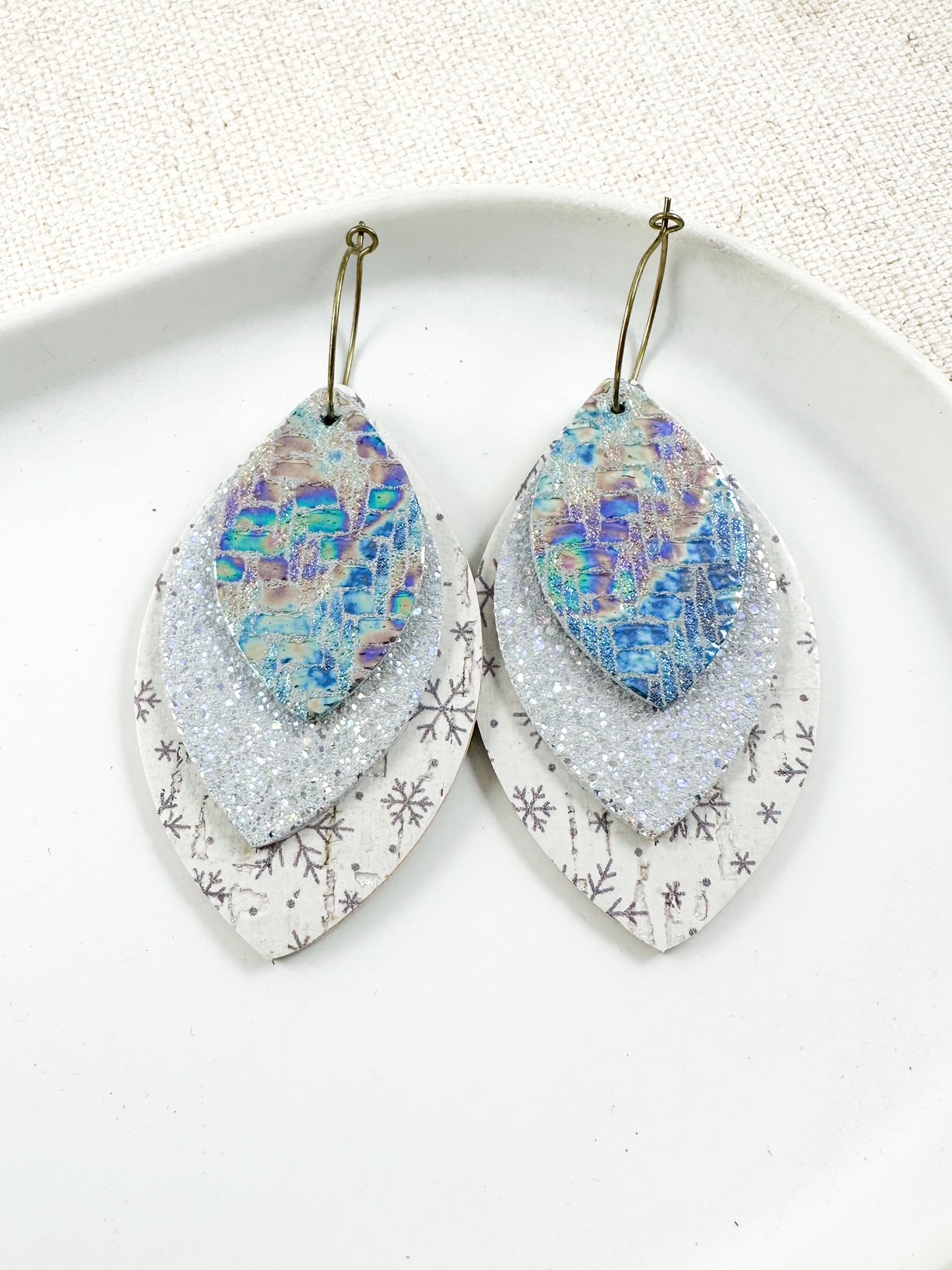 Layered iridescent leather drop earrings in silver and blue tones with removable leaf-shaped layers on gold-tone hoops.
