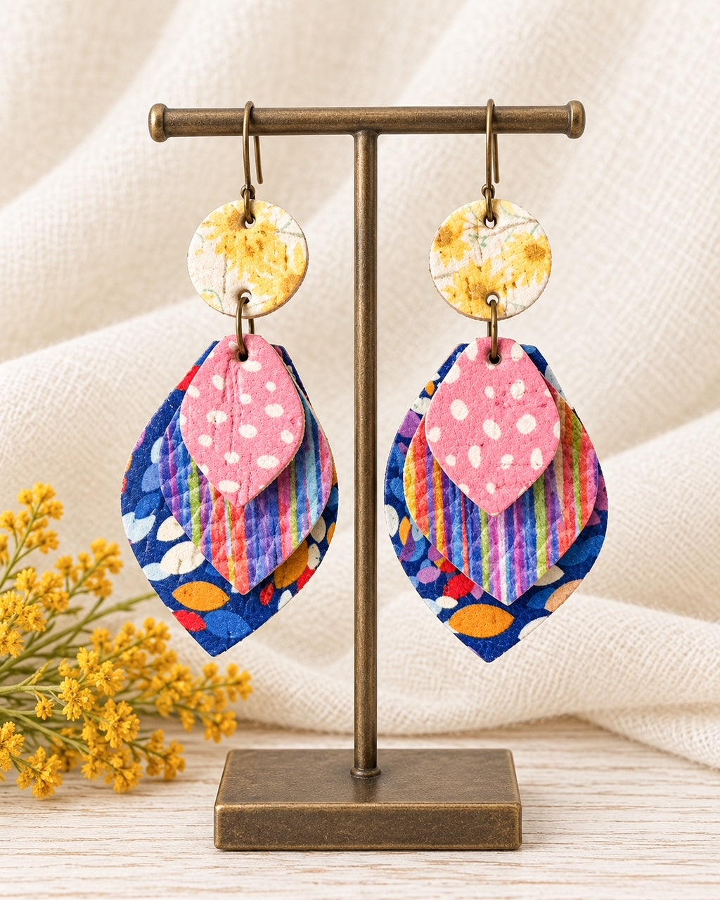 Something Good handmade leather earrings with colorful layered floral, striped and pink designs on an antique bronze stand