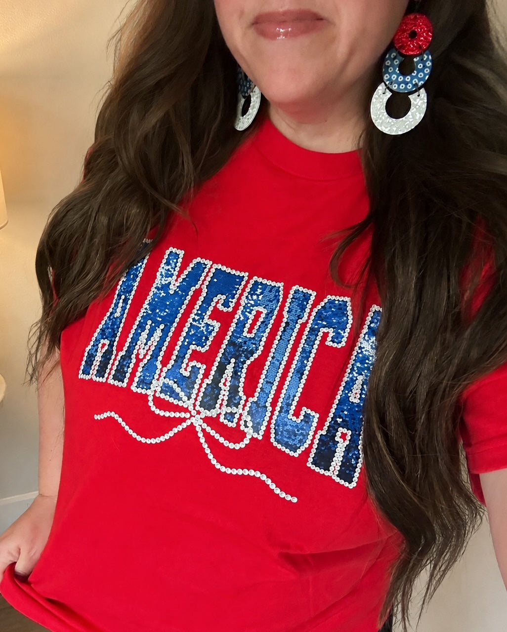 Sparkler Season Tee modeled with Firecracker Pop Earrings featuring a faux sequin America graphic on a red unisex Gildan tee.