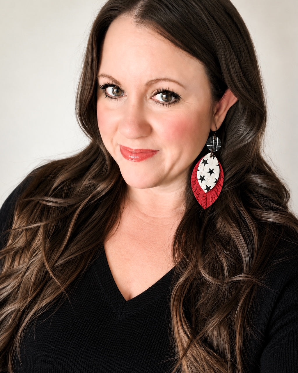 Woman with long brown hair modeling Starstruck Earrings featuring black-and-white plaid circles, white star-print layers, and textured red leather teardrops with a black V-neck top.
