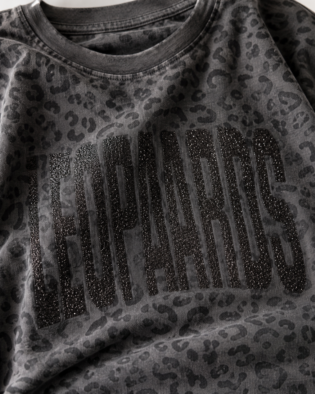Close-up of black leopard print shirt fabric and black glitter LEOPARDS graphic.