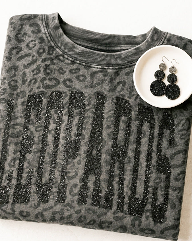 Black leopard print LEOPARDS graphic tee styled with coordinating earrings on a white jewelry dish.