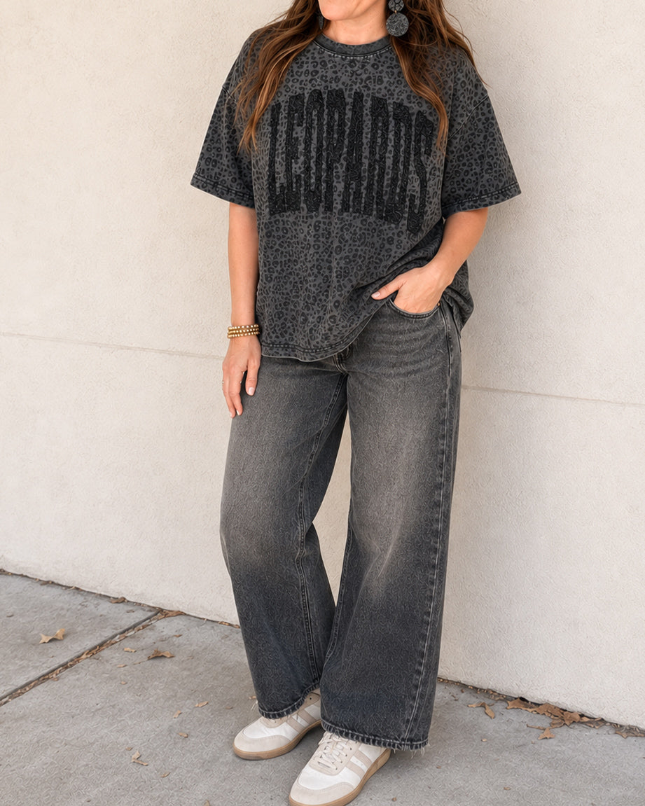 Woman wearing the black leopard print LEOPARDS graphic tee with relaxed jeans and white sneakers.