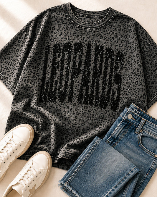 Black leopard print LEOPARDS graphic tee styled with medium-wash jeans and white sneakers.