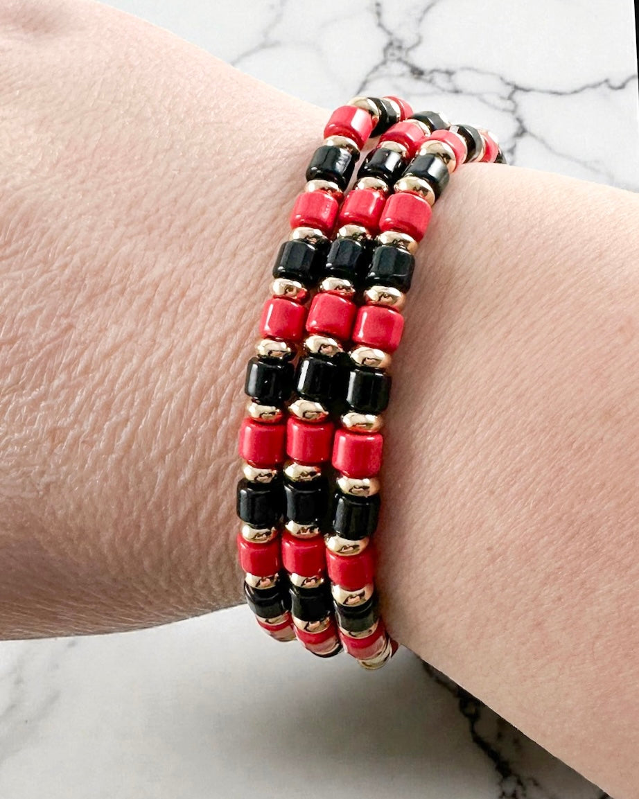 Red and black beaded bracelet trio with gold metal bead details shown layered as a stacked bracelet set.