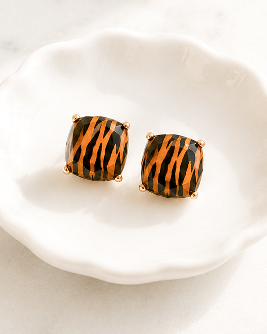 Tiger Trail tiger print stud earrings with faceted orange and black stones resting in a white shell-shaped jewelry dish.