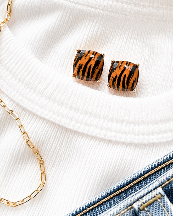 Tiger Trail tiger print stud earrings styled on a white sweater with denim and a gold chain for football game day.