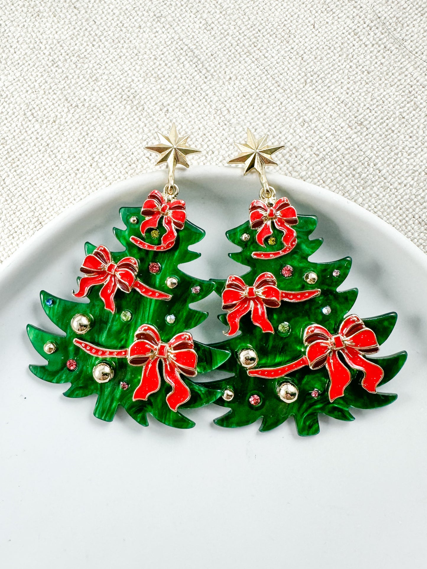 Green Christmas tree earrings with red bows, gold accents, and star stud posts on a white background