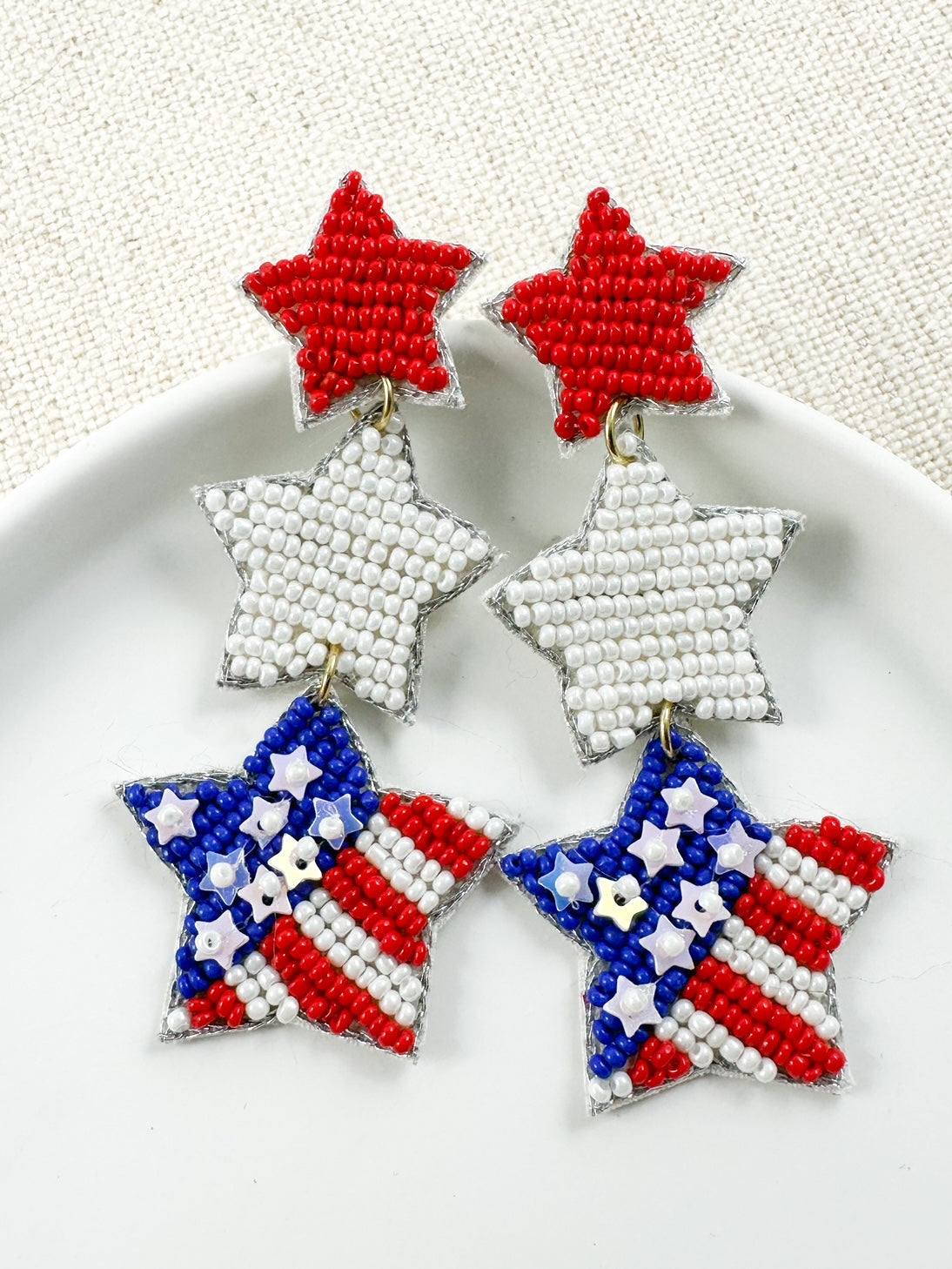 Under the Stars patriotic seed bead earrings with red white and blue star design on white jewelry dish