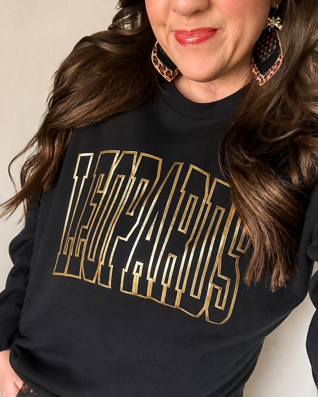 Woman wearing the black Varsity Edit Leopards sweatshirt with metallic-gold lettering