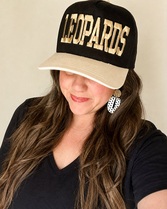 Woman wearing the Varsity Leopard Hat with a black V-neck tee and black-and-white polka-dot earrings
