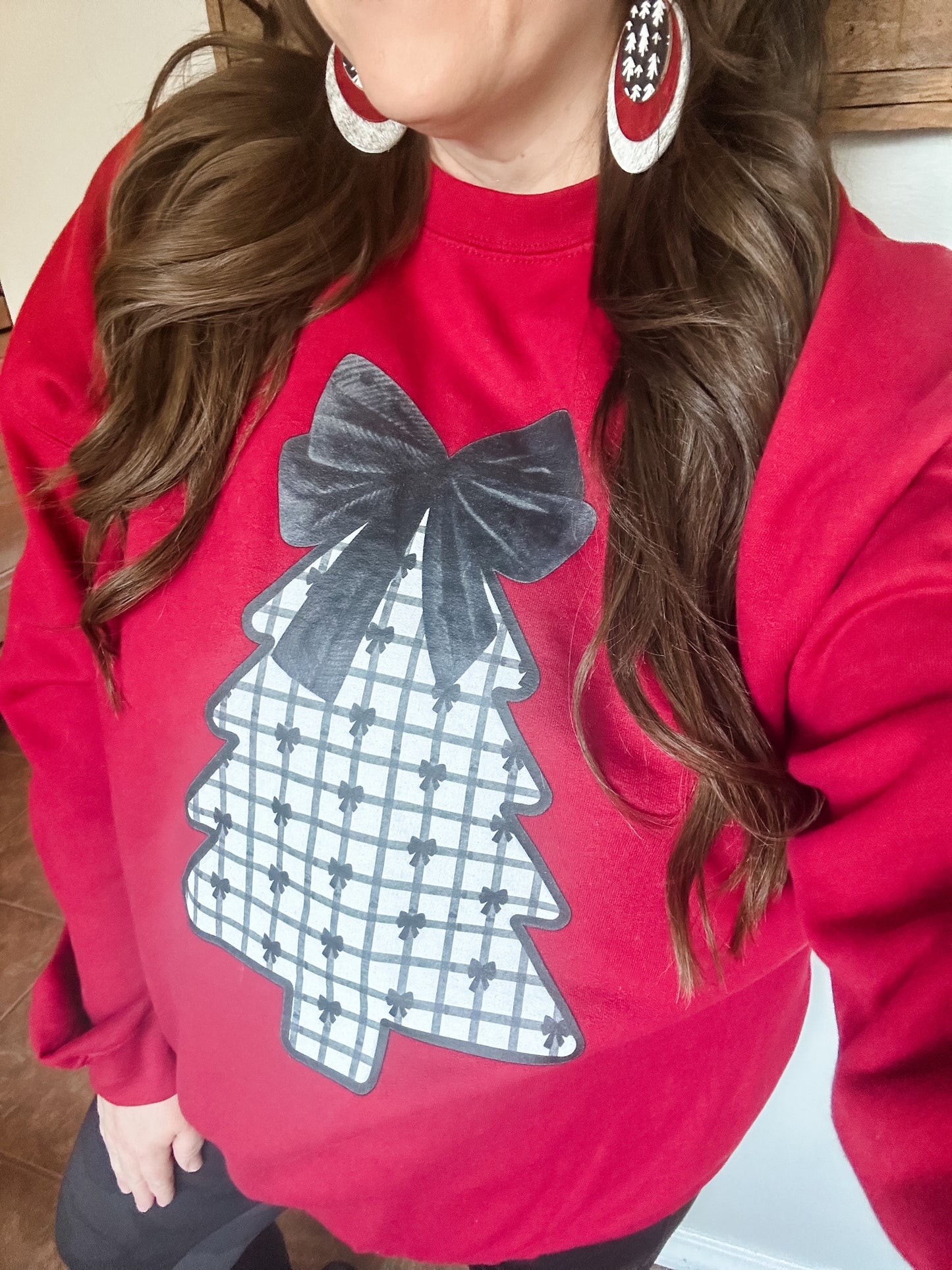 Woman wearing the Velvet Pines Sweatshirt and red statement earrings, featuring the plaid Christmas tree and black velvet bow design.