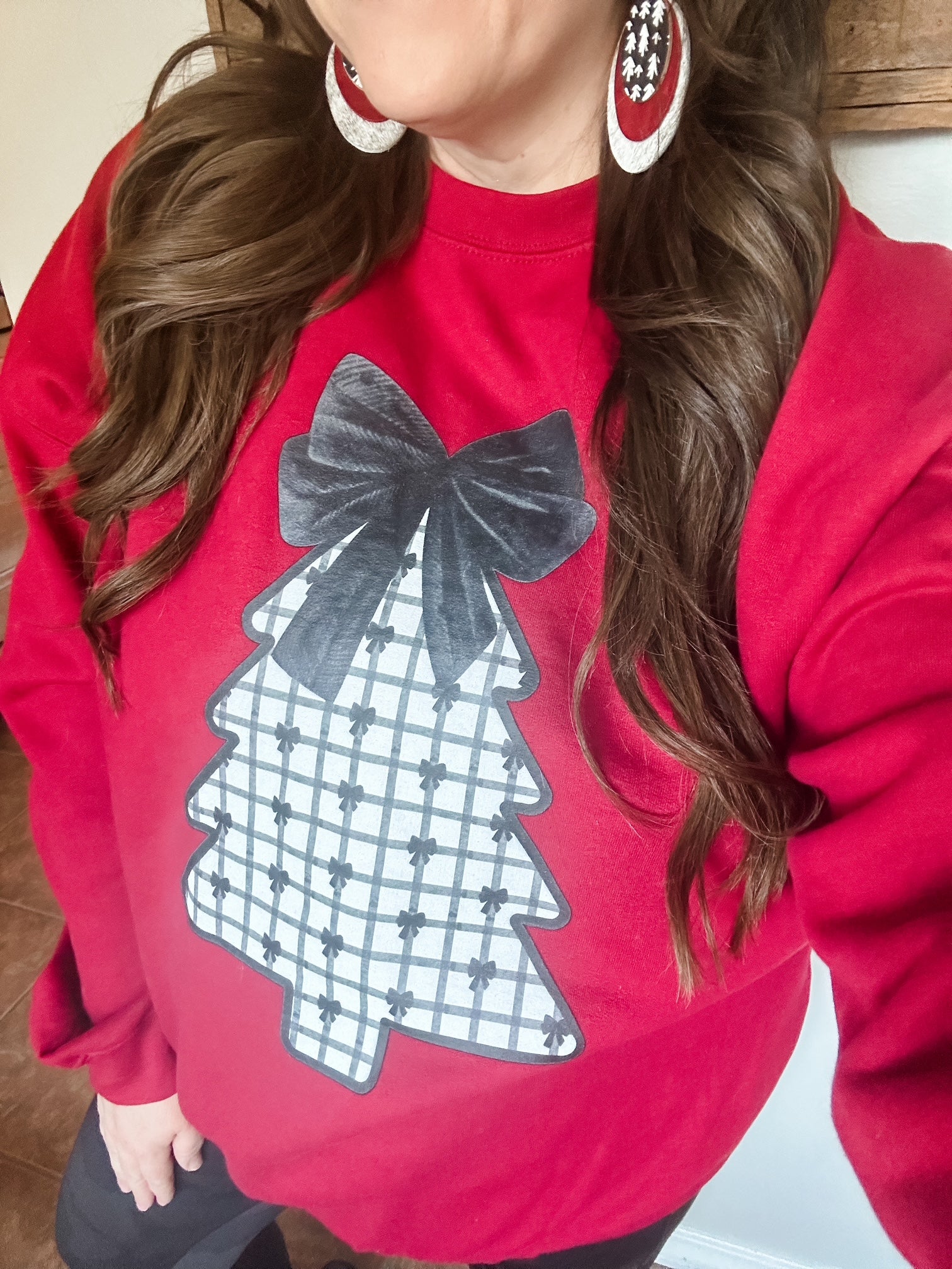 Woman wearing the Velvet Pines Sweatshirt and red statement earrings, featuring the plaid Christmas tree and black velvet bow design.