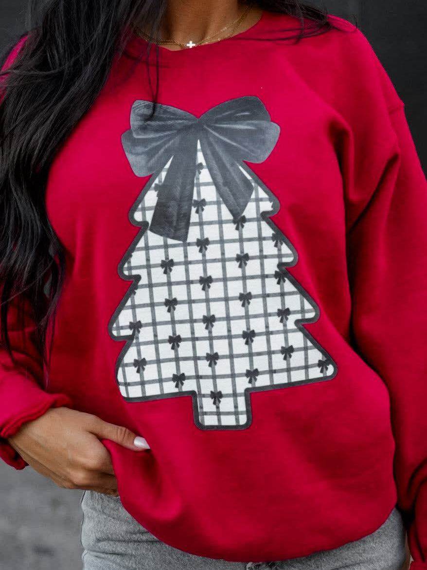 Model wearing the Velvet Pines Sweatshirt, showing a red sweatshirt with a plaid Christmas tree and black velvet bow detail.