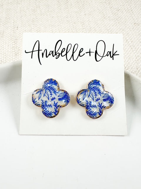 Blue and white floral clover-shaped stud earrings with gold trim on Anabelle+Oak backing card