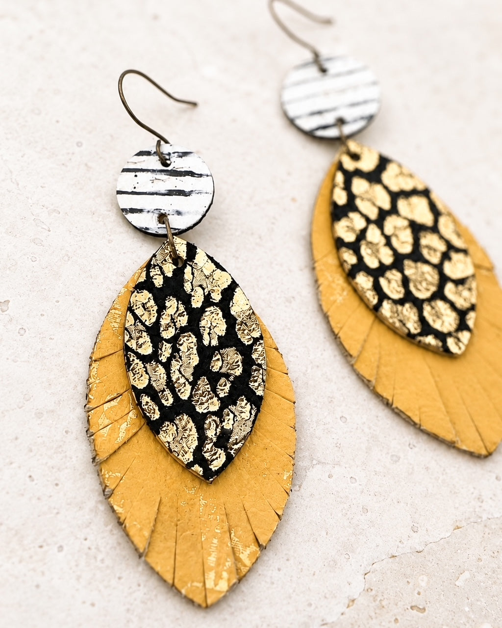 Close-up of the handmade Wild Card Earrings showing layered leather, hand-distressed edges, and antique-bronze-tone ear wires