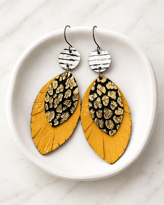 Wild Card Earrings arranged in a white dish, featuring black-and-white stripes, metallic-gold leopard print, and distressed yellow leather