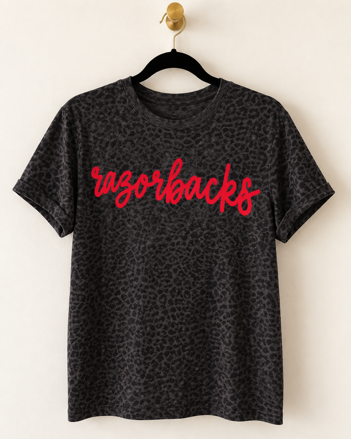 Dark leopard print Wild Script Tee hanging on a wooden hanger with custom script lettering across the front.